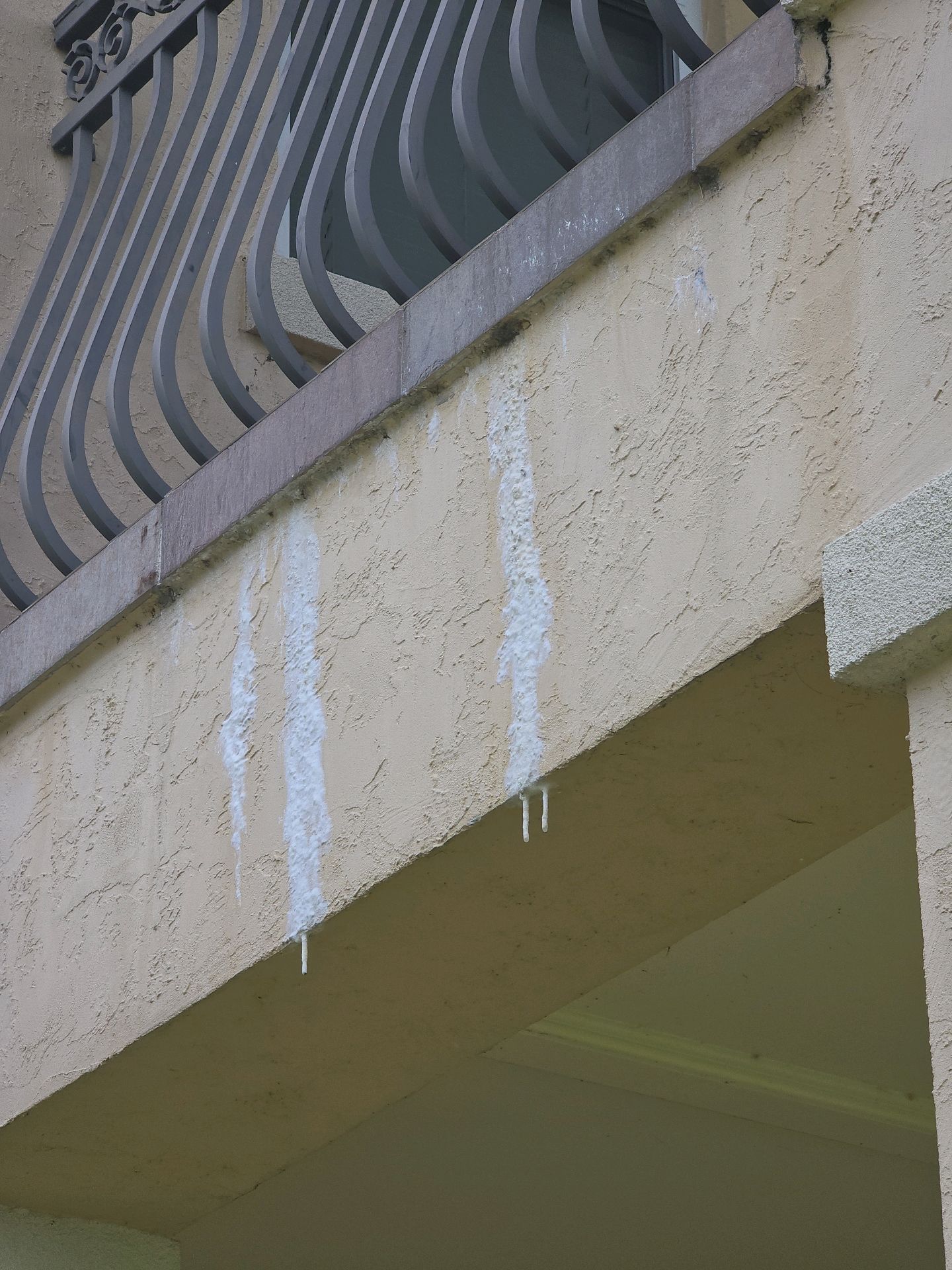 White mineral water staining running down a stucco wall below a second-floor balcony edge
