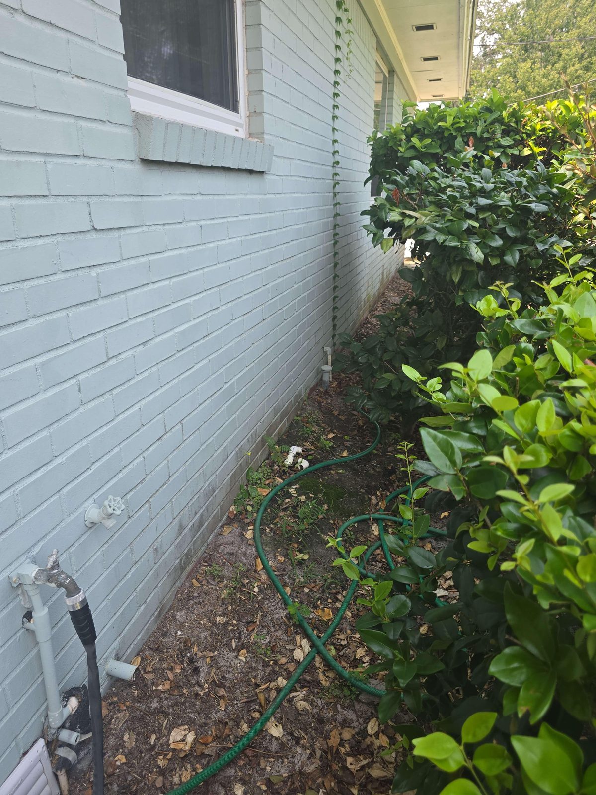 A metal vent pipe rising a few inches above bare soil along the exterior side wall of a house.